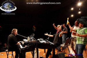 Dueling pianos performance with energetic crowd cheering on stage.