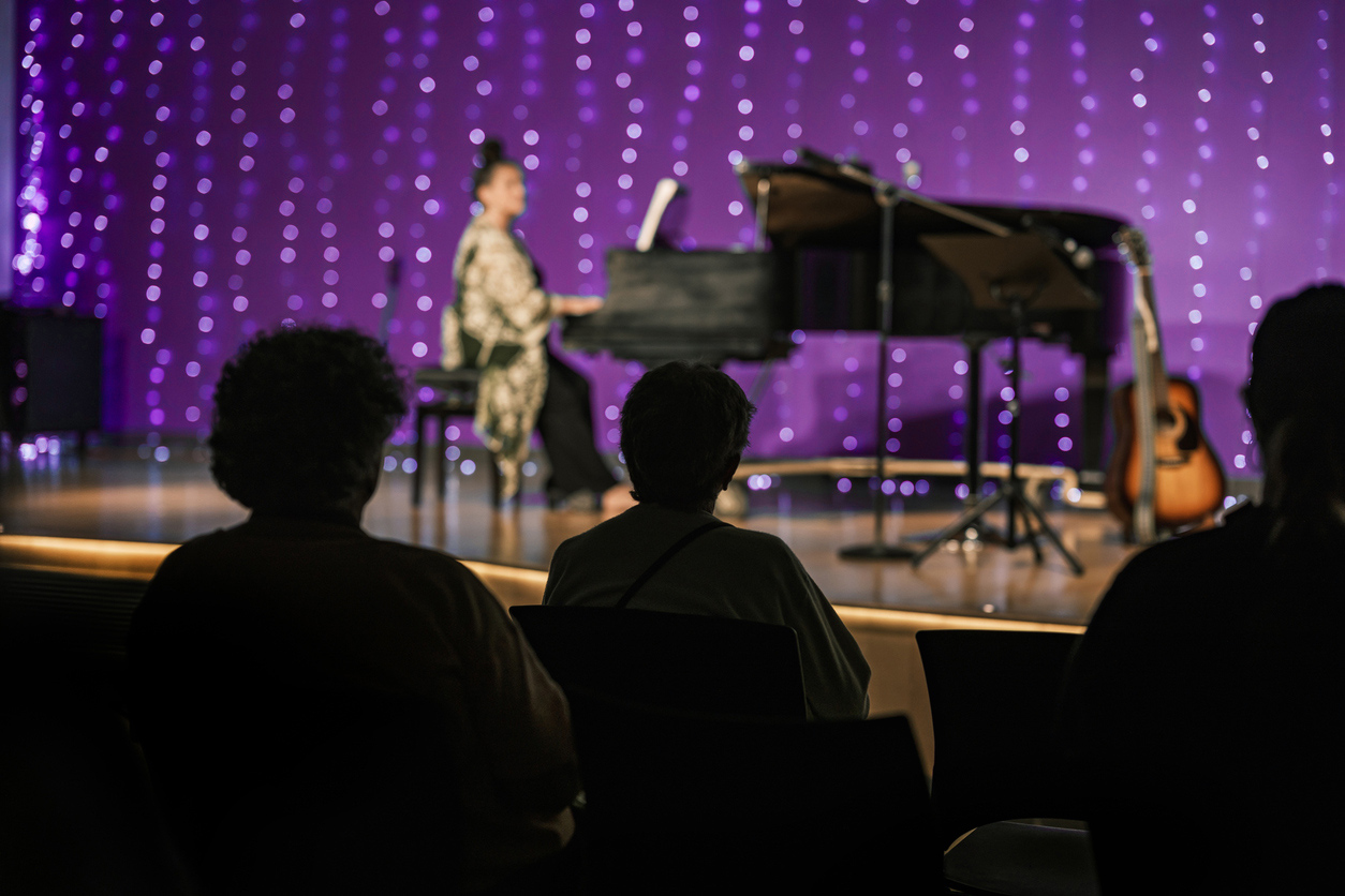 A person playing piano on stage with purple lights in background.