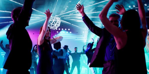 People dancing energetically at a vibrant nightclub with colorful lights.