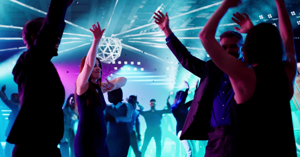 People dancing energetically at a vibrant nightclub with colorful lights.