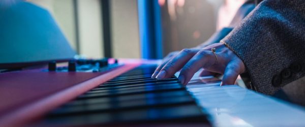 A person playing keyboard piano with a focus on their hand and the keys.