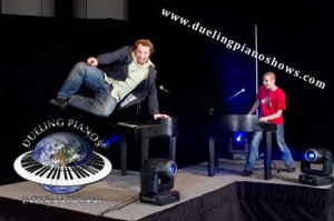Man jumps off a piano during dueling piano show performance on stage.