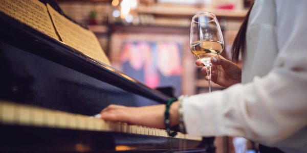A woman playing piano with a glass of white wine in hand.