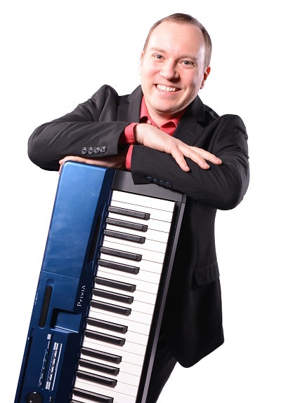 A smiling person leaning on a blue keyboard, wearing a suit and red shirt.